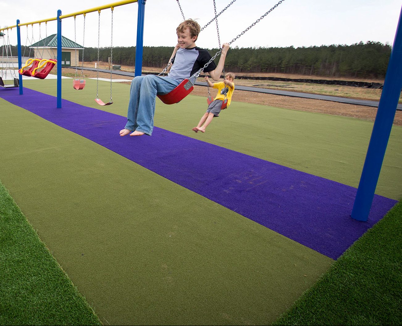 Kids playing on swing set with SYNLawn artificial playground grass